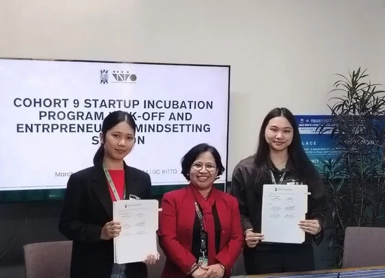 Three women holding papers in front of a slide for the Cohort 9 startup incubation program kick-off.